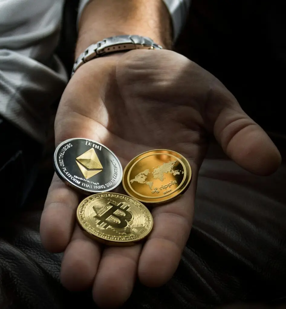 Hand holding Bitcoin, Ethereum, and Ripple coins representing digital currency.